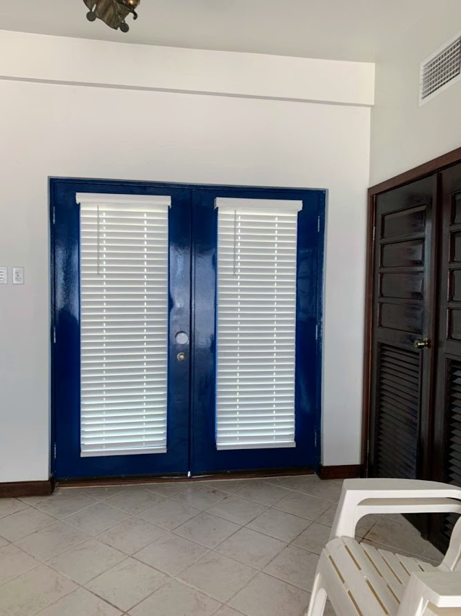 Modelo de distribuidor tropical de tamaño medio con paredes blancas, suelo de baldosas de porcelana, puerta doble, puerta azul, suelo beige y vigas vistas