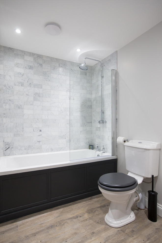 Photo of a large scandinavian kids bathroom in Wiltshire with shaker cabinets, black cabinets, a drop-in tub, a shower/bathtub combo, a two-piece toilet, gray tile, marble, grey walls, linoleum floors and a console sink.