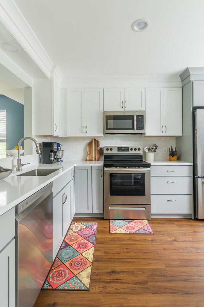 Small transitional l-shaped medium tone wood floor and brown floor eat-in kitchen photo in Detroit with an undermount sink, shaker cabinets, white cabinets, quartz countertops, white backsplash, subway tile backsplash, stainless steel appliances, an island and white countertops
