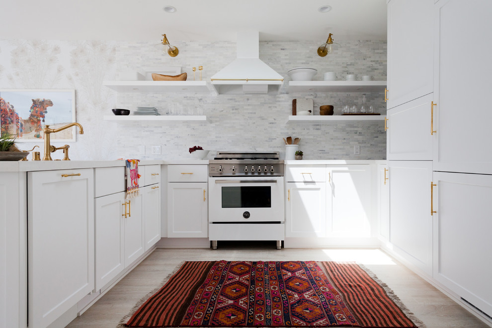 Inspiration for a mid-sized coastal u-shaped light wood floor open concept kitchen remodel in Los Angeles with a drop-in sink, recessed-panel cabinets, white cabinets, marble countertops, white backsplash, porcelain backsplash, white appliances and no island