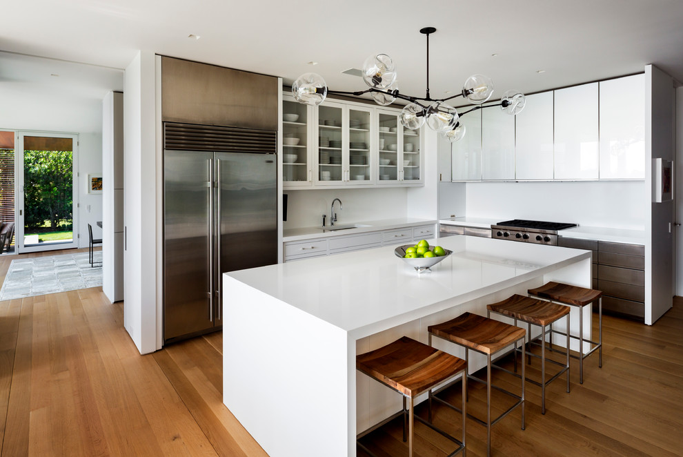 Contemporary l-shaped kitchen in New York with an undermount sink, white cabinets, white splashback, stainless steel appliances, medium hardwood floors and with island.