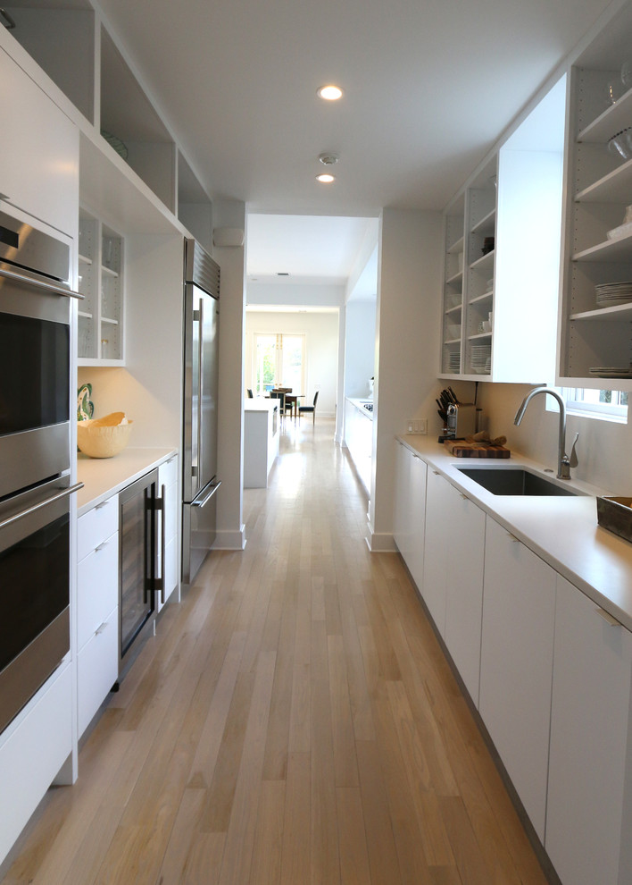 Large contemporary u-shaped kitchen in New Orleans with an undermount sink, flat-panel cabinets, white cabinets, marble benchtops, white splashback, stainless steel appliances, light hardwood floors, with island and white benchtop.