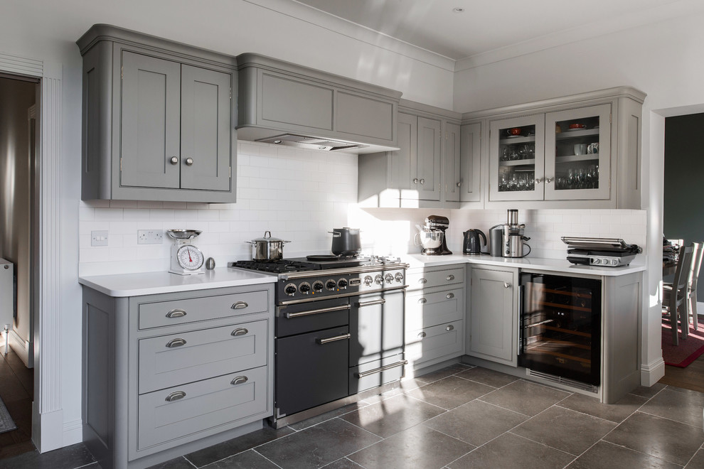 This is an example of a mid-sized contemporary u-shaped open plan kitchen in Kent with shaker cabinets, a farmhouse sink, grey cabinets, quartzite benchtops, white splashback, subway tile splashback, black appliances, limestone floors, grey floor and white benchtop.