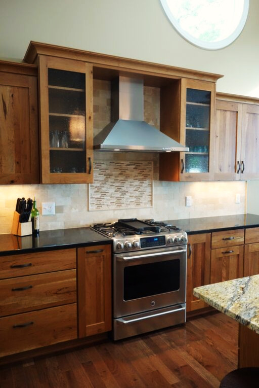 Inspiration for a rustic l-shaped dark wood floor eat-in kitchen remodel with recessed-panel cabinets, medium tone wood cabinets, granite countertops, beige backsplash, stone tile backsplash, stainless steel appliances and an island