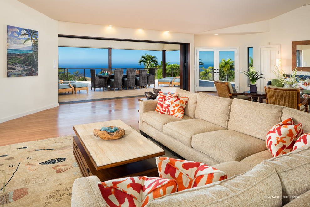Large tropical open concept living room in Hawaii with white walls, light hardwood floors, no fireplace, no tv and brown floor.