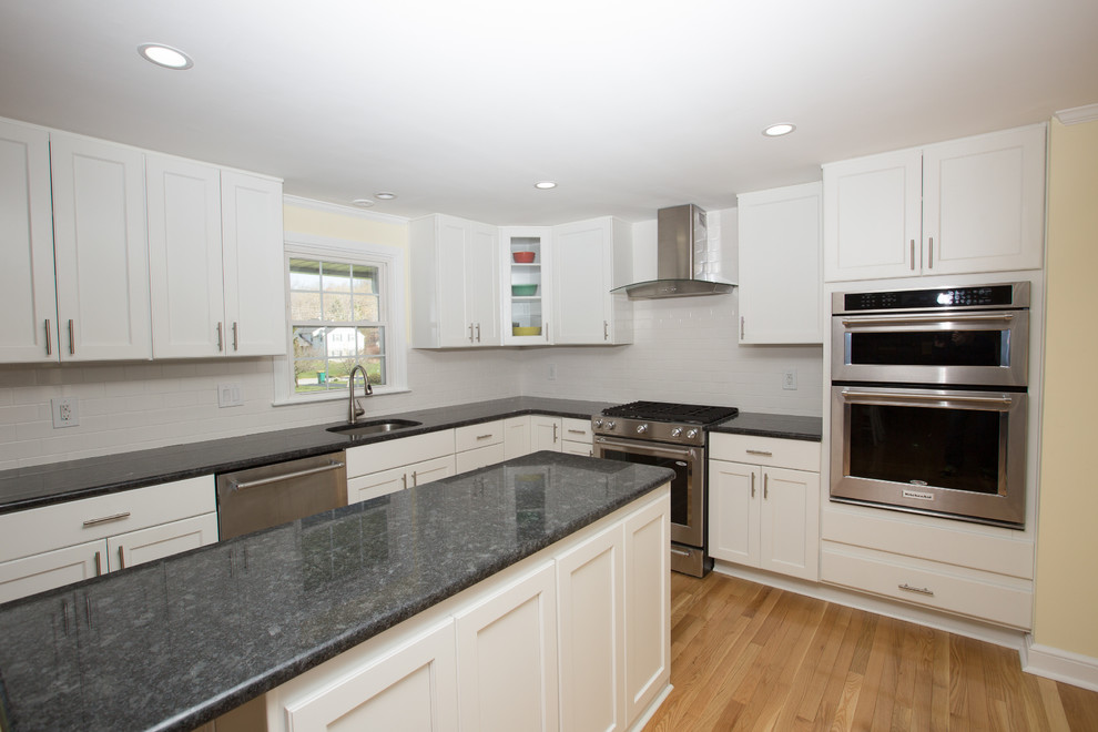 This is an example of a mid-sized contemporary u-shaped eat-in kitchen in Philadelphia with a double-bowl sink, recessed-panel cabinets, white cabinets, granite benchtops, white splashback, subway tile splashback, stainless steel appliances, medium hardwood floors and with island.