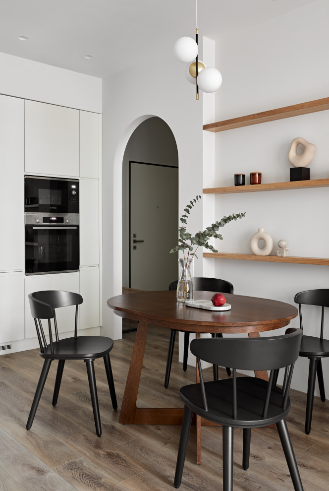 Photo of a mid-sized contemporary single-wall eat-in kitchen in Saint Petersburg with flat-panel cabinets, white cabinets, solid surface benchtops, white splashback, engineered quartz splashback, black appliances, medium hardwood floors, brown floor and white benchtop.