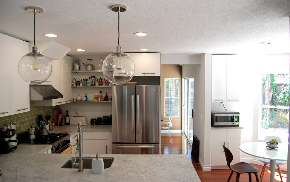 Photo of a modern u-shaped eat-in kitchen in Los Angeles with stainless steel appliances, a single-bowl sink, flat-panel cabinets, white cabinets, marble benchtops, green splashback and subway tile splashback.