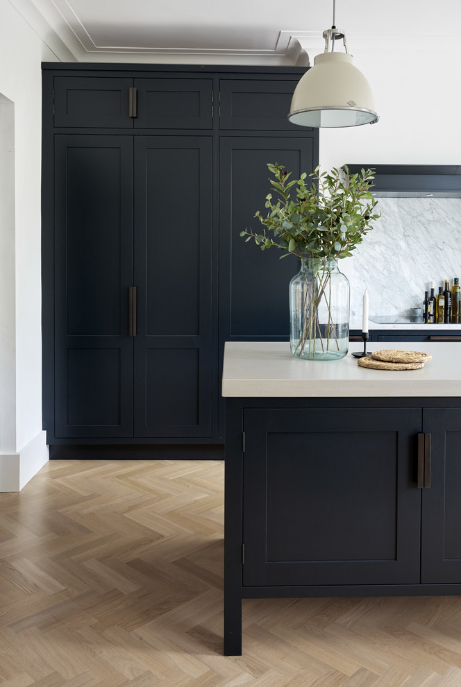 Inspiration for a large country galley eat-in kitchen in London with an integrated sink, shaker cabinets, blue cabinets, concrete benchtops, white splashback, marble splashback, panelled appliances, light hardwood floors, with island, beige floor and white benchtop.