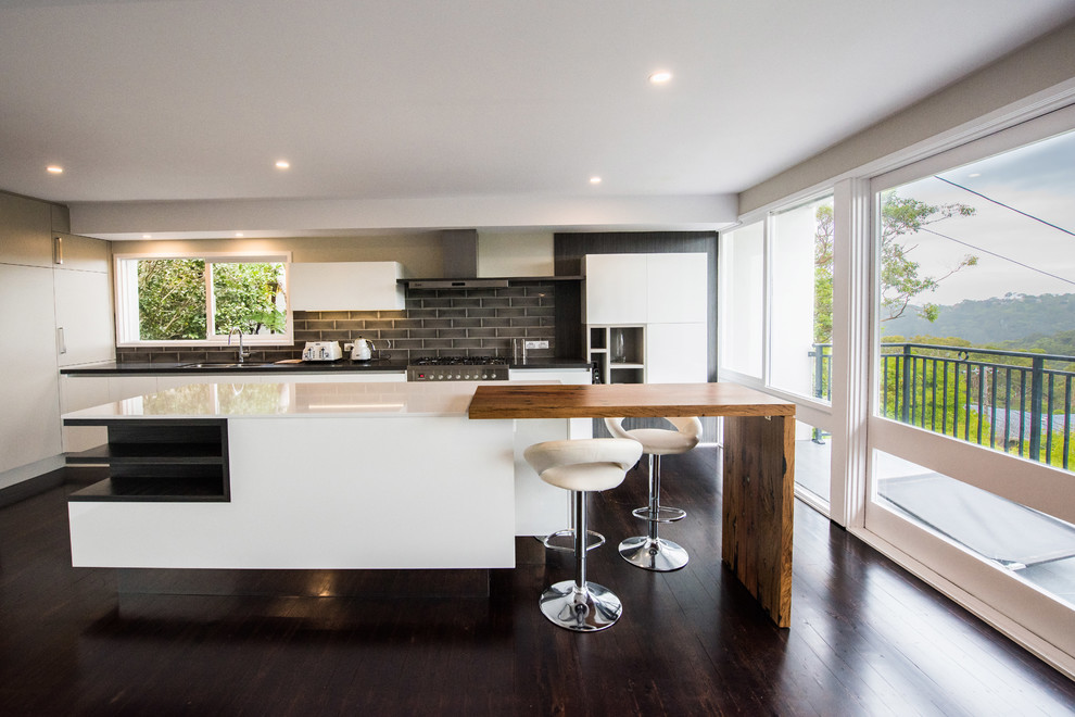 Inspiration for a large contemporary l-shaped eat-in kitchen in Sydney with a drop-in sink, wood benchtops, black splashback, ceramic splashback, stainless steel appliances, dark hardwood floors, with island, flat-panel cabinets, white cabinets and white benchtop.
