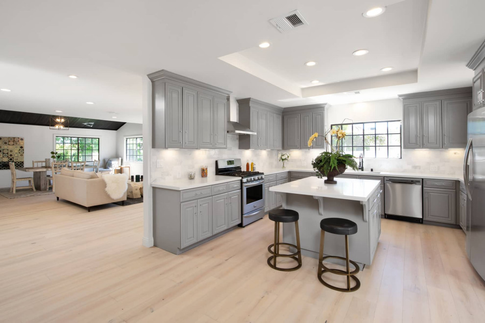 Design ideas for a large midcentury u-shaped eat-in kitchen in Los Angeles with an undermount sink, raised-panel cabinets, grey cabinets, marble benchtops, white splashback, marble splashback, stainless steel appliances, light hardwood floors, with island, white benchtop and recessed.