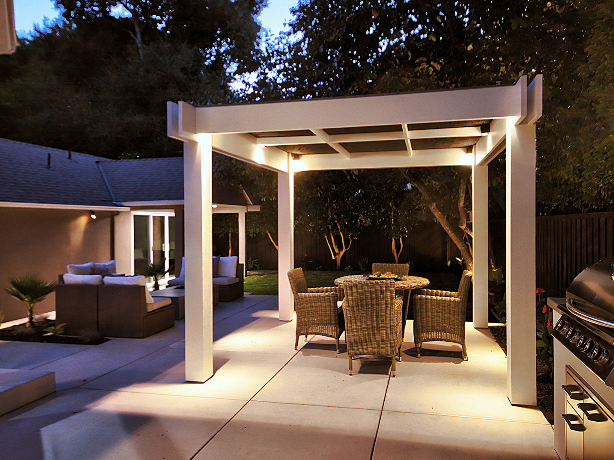 Serene Nighttime Backyard with Pergola and Uplighted Trees