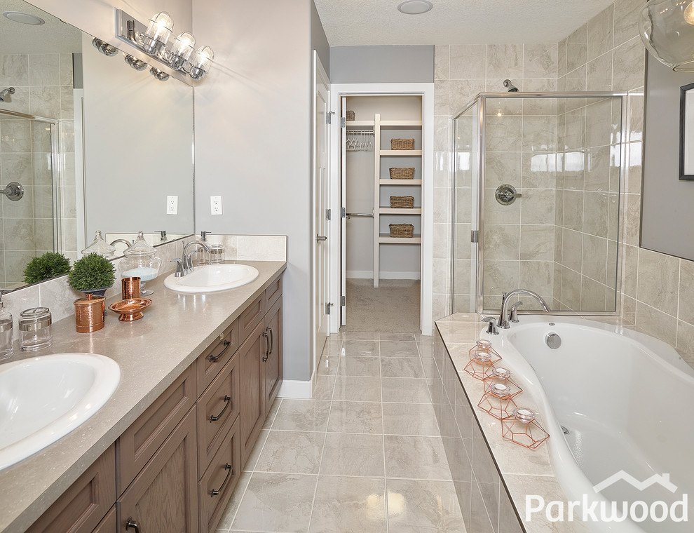 Photo of a mid-sized industrial master bathroom in Edmonton with recessed-panel cabinets, medium wood cabinets, laminate benchtops, a drop-in tub, a two-piece toilet, gray tile, ceramic tile, grey walls and ceramic floors.