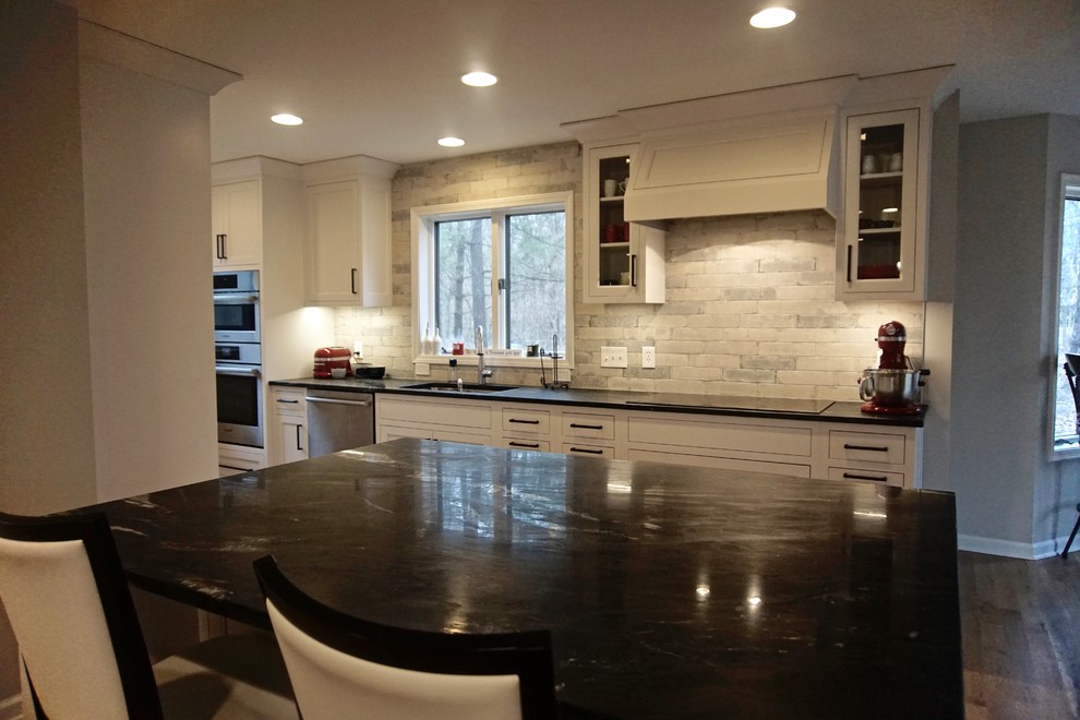 Example of a large transitional medium tone wood floor open concept kitchen design in Indianapolis with an undermount sink, beaded inset cabinets, white cabinets, soapstone countertops, white backsplash, stone slab backsplash, stainless steel appliances and an island