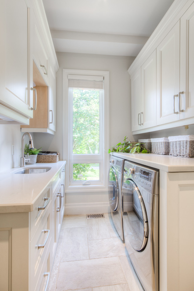 Inspiration for a mid-sized transitional galley dedicated laundry room in Toronto with an undermount sink, recessed-panel cabinets, white cabinets, limestone benchtops, beige walls, porcelain floors, a side-by-side washer and dryer, beige floor and white benchtop.