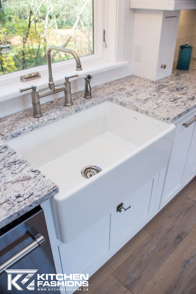 Large transitional u-shaped light wood floor eat-in kitchen photo with a farmhouse sink, shaker cabinets, white cabinets, granite countertops, white backsplash, subway tile backsplash, stainless steel appliances and no island