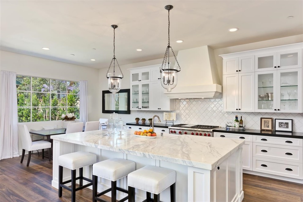 Eat-in kitchen - large mediterranean galley medium tone wood floor eat-in kitchen idea in San Diego with a farmhouse sink, shaker cabinets, white cabinets, white backsplash, stainless steel appliances, an island and marble countertops