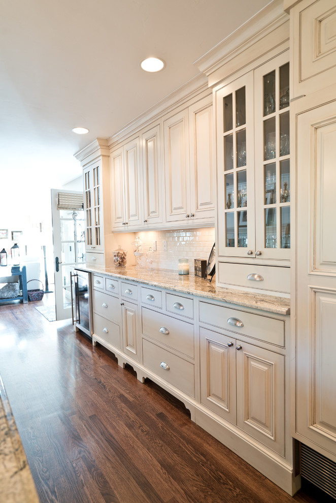 This is an example of an expansive traditional u-shaped eat-in kitchen in Denver with a farmhouse sink, raised-panel cabinets, white cabinets, granite benchtops, white splashback, ceramic splashback, panelled appliances, dark hardwood floors, with island, brown floor and beige benchtop.