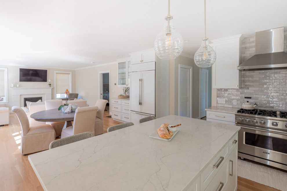 Inspiration for a huge transitional l-shaped light wood floor and brown floor open concept kitchen remodel in Boston with an undermount sink, shaker cabinets, white cabinets, quartz countertops, gray backsplash, subway tile backsplash, stainless steel appliances, an island and white countertops