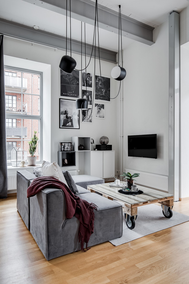 Design ideas for a mid-sized industrial living room in Gothenburg with white walls, medium hardwood floors, no fireplace, a wall-mounted tv and brown floor.