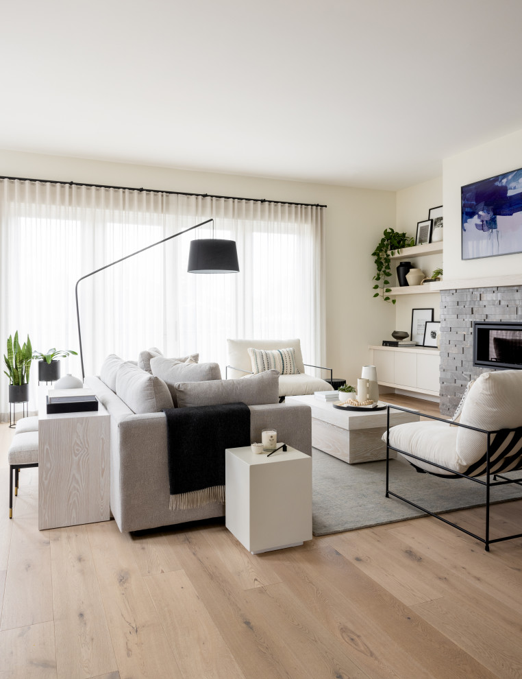 На фото: открытая гостиная комната среднего размера в стиле модернизм с белыми стенами, светлым паркетным полом, стандартным камином, фасадом камина из каменной кладки, телевизором на стене и бежевым полом