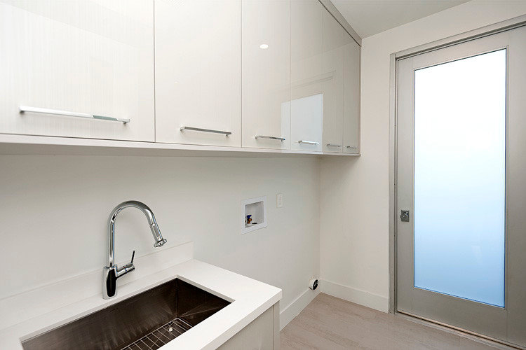 Photo of a small contemporary u-shaped laundry room in Orange County with an undermount sink, white cabinets, quartz benchtops, white walls, porcelain floors and flat-panel cabinets.