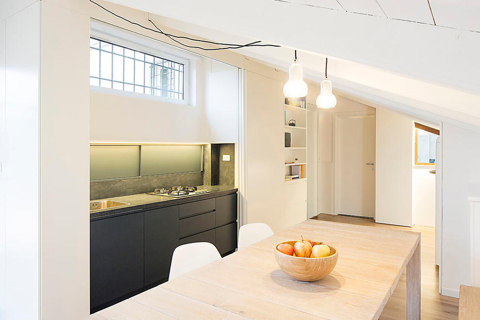 This is an example of a small contemporary single-wall eat-in kitchen in Bologna with a drop-in sink, flat-panel cabinets, black cabinets and light hardwood floors.