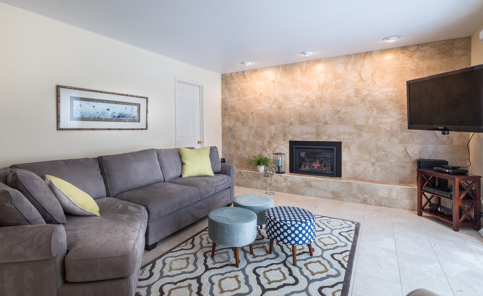 Photo of a large transitional open concept family room with beige walls, marble floors, a standard fireplace, a tile fireplace surround, a wall-mounted tv and beige floor.
