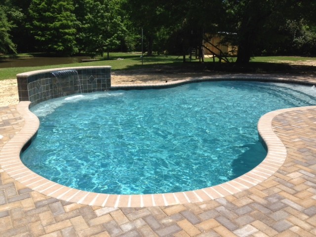 Mid-sized traditional backyard custom-shaped natural pool in New Orleans with a water feature and brick pavers.