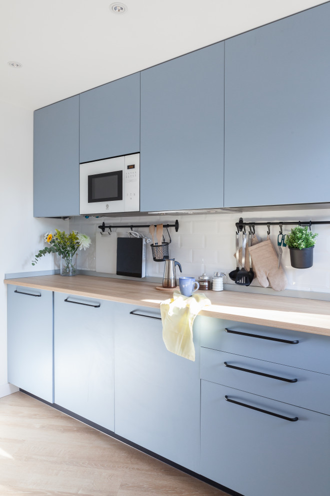 Design ideas for a small scandinavian single-wall open plan kitchen in Other with a farmhouse sink, flat-panel cabinets, blue cabinets, laminate benchtops, white splashback, ceramic splashback, white appliances, laminate floors, no island, brown floor and brown benchtop.