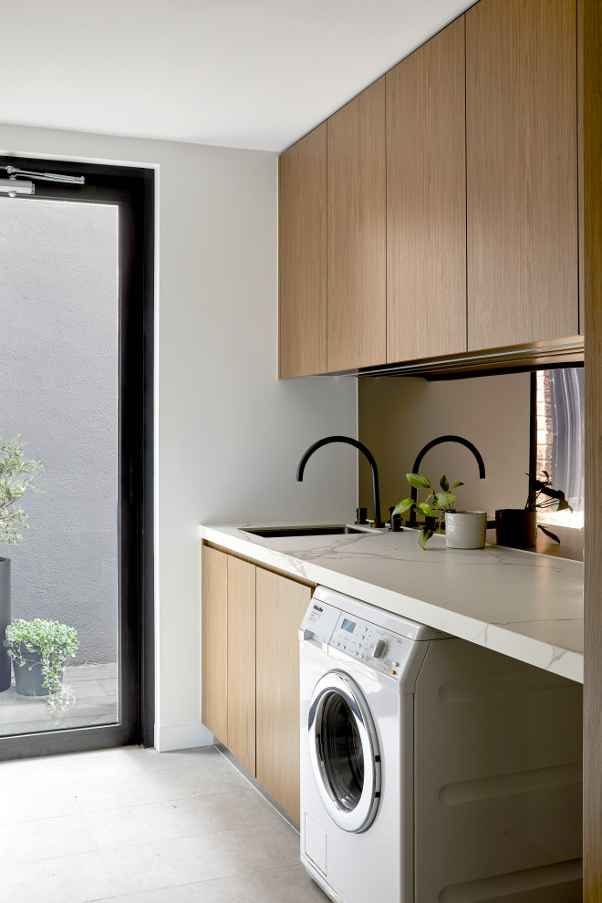 Large contemporary single-wall dedicated laundry room in Melbourne with an undermount sink, flat-panel cabinets, medium wood cabinets, marble benchtops, metallic splashback, metal splashback, white walls, porcelain floors, a side-by-side washer and dryer, grey floor and white benchtop.
