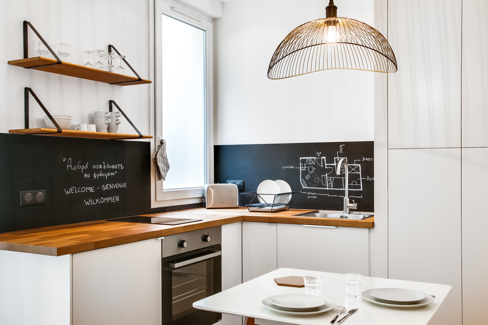 Inspiration for a small contemporary l-shaped eat-in kitchen in Paris with a drop-in sink, flat-panel cabinets, white cabinets, wood benchtops, black splashback, black appliances and no island.