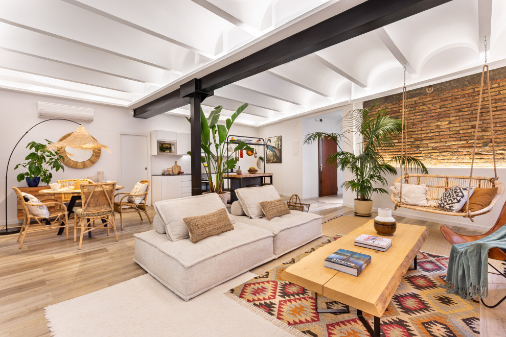 Photo of a large tropical loft-style family room in Barcelona with a home bar, blue walls, light hardwood floors, no fireplace, a freestanding tv, beige floor, vaulted and brick walls.