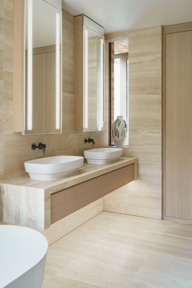 Design ideas for a mid-sized contemporary master bathroom in London with flat-panel cabinets, beige cabinets, a freestanding tub, a curbless shower, a wall-mount toilet, beige tile, travertine, beige walls, travertine floors, a vessel sink, marble benchtops, beige floor, a hinged shower door, beige benchtops, a double vanity and a floating vanity.
