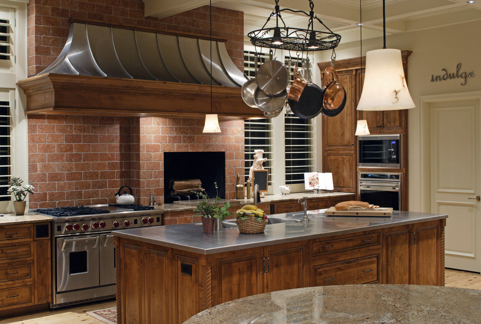 This is an example of a mid-sized country l-shaped eat-in kitchen in Omaha with an undermount sink, raised-panel cabinets, medium wood cabinets, quartz benchtops, red splashback, brick splashback, stainless steel appliances, light hardwood floors, multiple islands and beige floor.