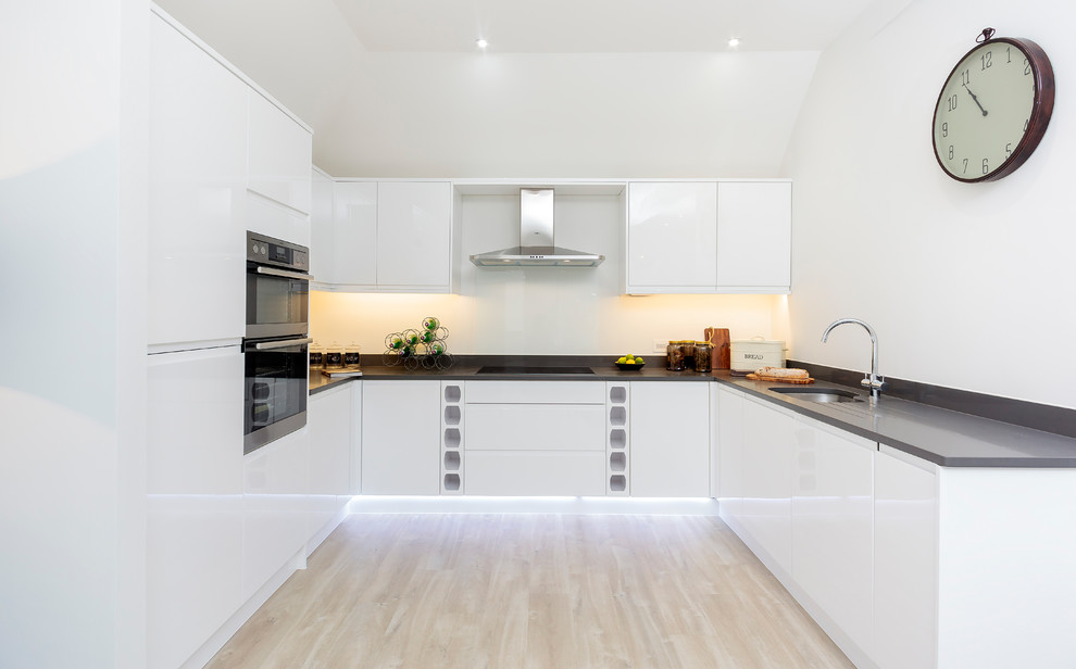 Photo of a contemporary u-shaped kitchen in Dorset with an undermount sink, flat-panel cabinets, white cabinets, solid surface benchtops and no island.
