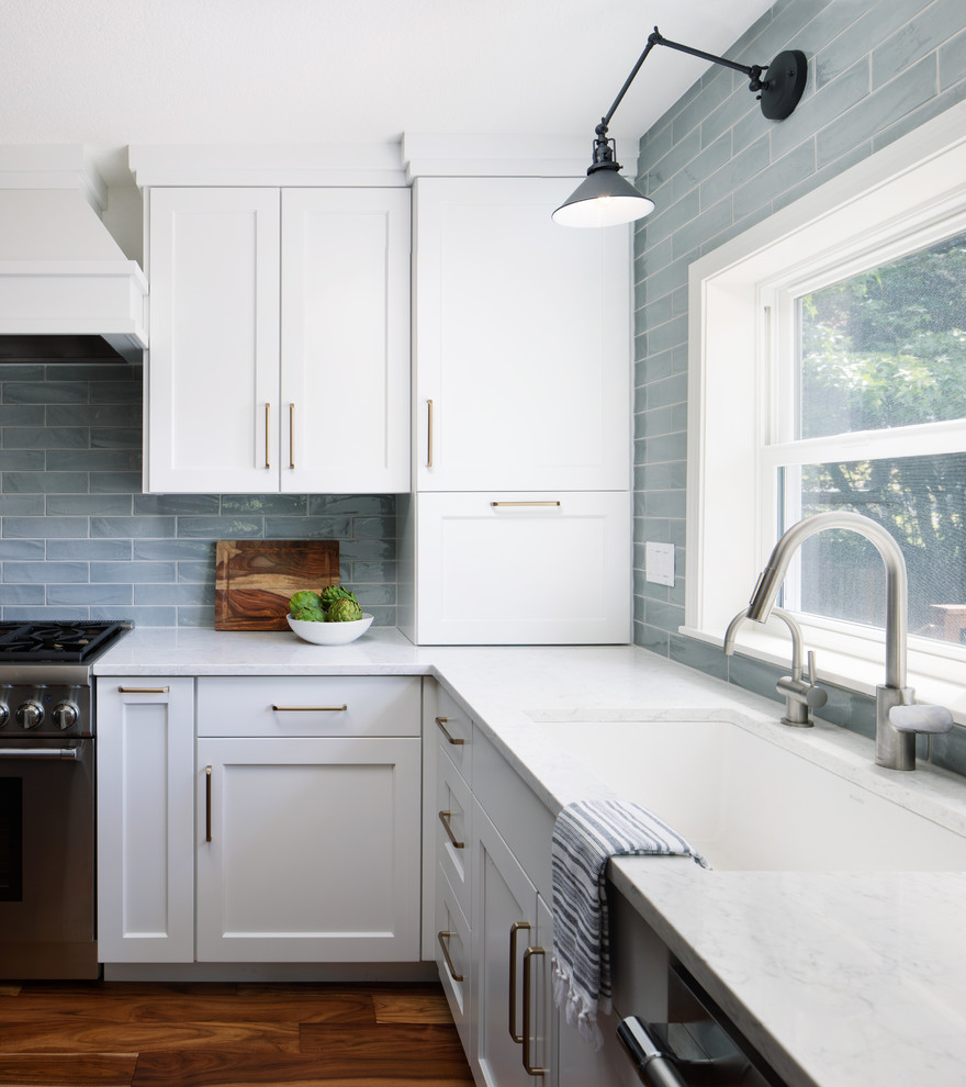 Mid-sized trendy l-shaped medium tone wood floor and brown floor open concept kitchen photo in Portland with an undermount sink, shaker cabinets, white cabinets, quartz countertops, blue backsplash, ceramic backsplash, stainless steel appliances, an island and white countertops