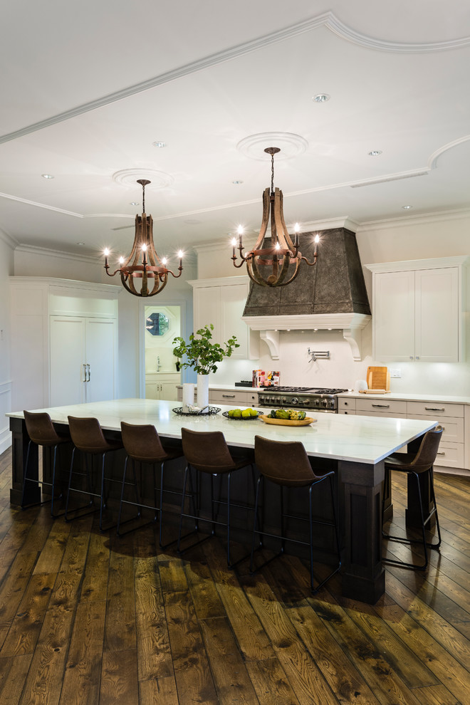 Huge mountain style u-shaped medium tone wood floor and brown floor open concept kitchen photo in Vancouver with an undermount sink, shaker cabinets, white cabinets, solid surface countertops, white backsplash, stone slab backsplash, stainless steel appliances, an island and white countertops