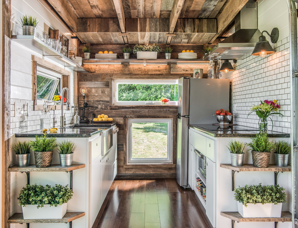 Inspiration for an industrial galley open plan kitchen in Nashville with a farmhouse sink, flat-panel cabinets, white cabinets, white splashback, subway tile splashback, panelled appliances, dark hardwood floors, no island, brown floor and grey benchtop.