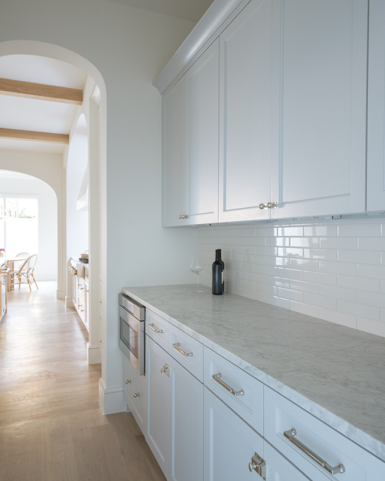 This is an example of a large coastal single-wall kitchen pantry in Dallas with a submerged sink, shaker cabinets, blue cabinets, marble worktops, white splashback, metro tiled splashback, stainless steel appliances, light hardwood flooring, an island, beige floors, grey worktops and exposed beams.