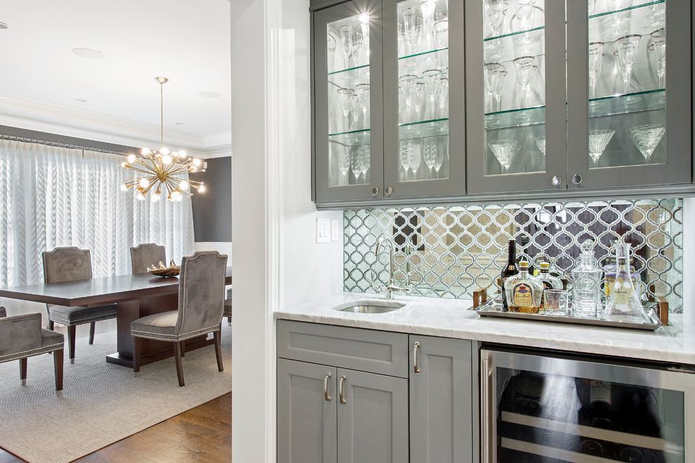 Transitional wet bar in New York with glass-front cabinets, grey cabinets, marble benchtops, mirror splashback, dark hardwood floors, an undermount sink and white benchtop.