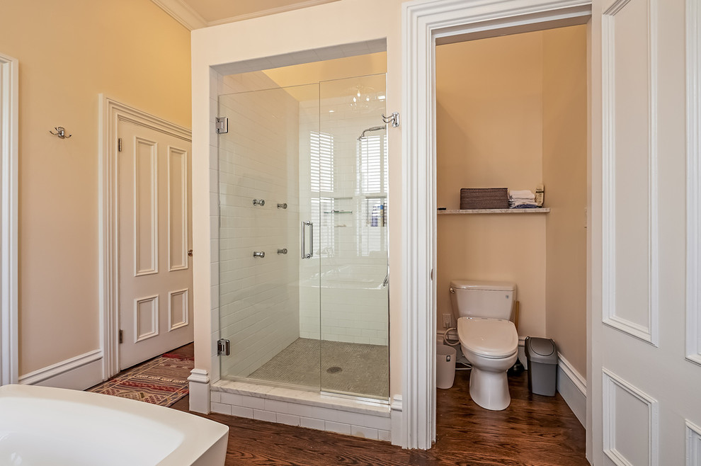 Inspiration for a mid-sized traditional master bathroom in Boston with red cabinets, a freestanding tub, an alcove shower, a two-piece toilet, beige walls, dark hardwood floors, an undermount sink, marble benchtops, beige floor and a hinged shower door.