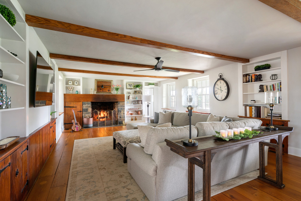 Large cottage medium tone wood floor, brown floor and exposed beam family room photo in Philadelphia with gray walls, a standard fireplace, a wood fireplace surround and a media wall