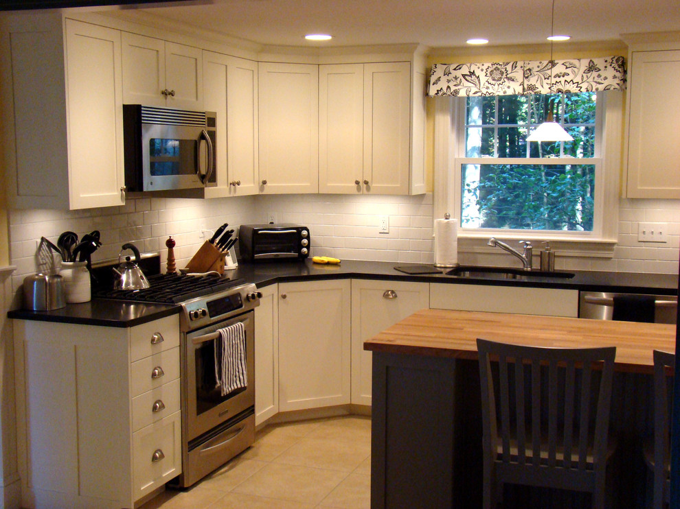 This is an example of a mid-sized contemporary l-shaped eat-in kitchen in Portland Maine with an undermount sink, shaker cabinets, white cabinets, wood benchtops, white splashback, subway tile splashback, stainless steel appliances, ceramic floors and with island.