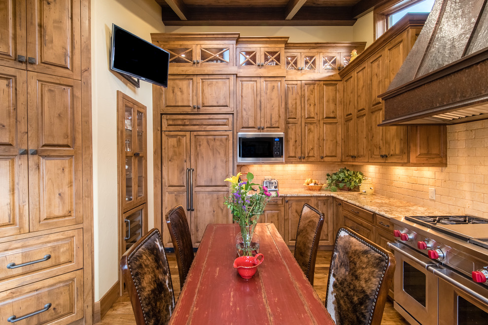 Example of a mountain style l-shaped medium tone wood floor and brown floor kitchen design in Denver with raised-panel cabinets, medium tone wood cabinets, white backsplash, brick backsplash and stainless steel appliances