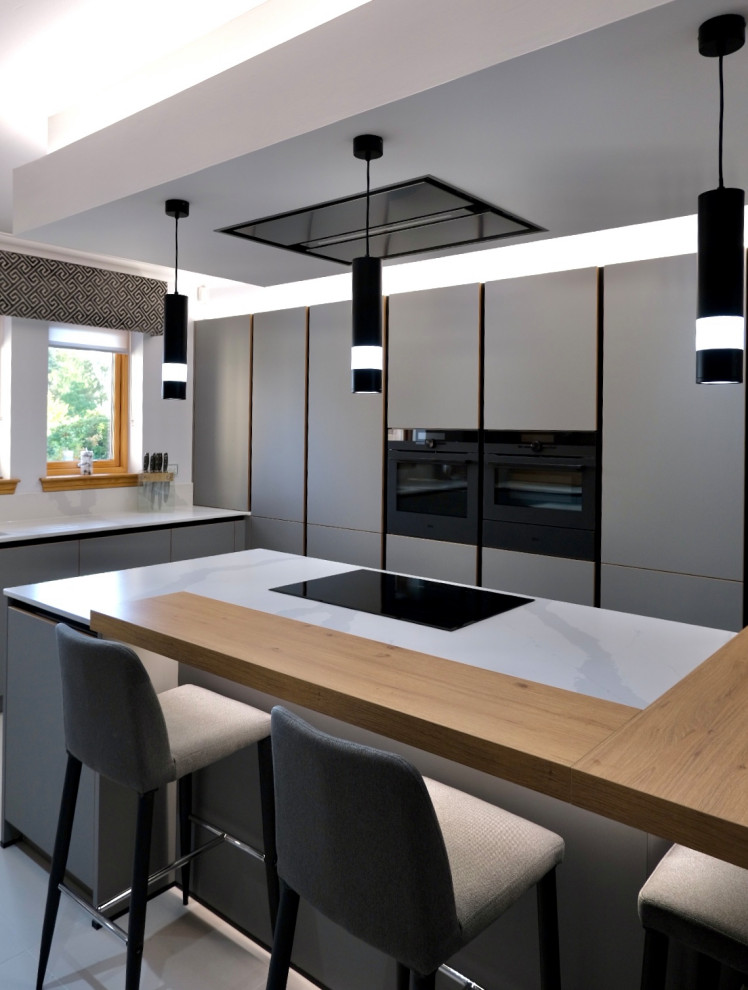 Источник вдохновения для домашнего уюта: большая кухня-гостиная в стиле модернизм с серыми фасадами, черной техникой, островом и белой столешницей