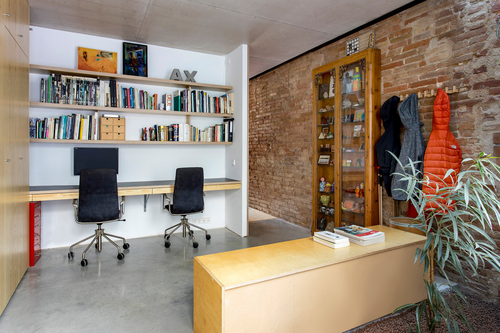 Photo of a mid-sized industrial study room in Barcelona with white walls, concrete floors, a built-in desk, grey floor and brick walls.