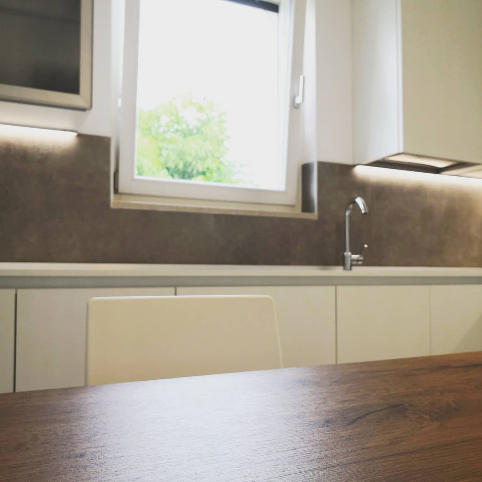 Bild på ett stort funkis vit vitt kök, med en nedsänkt diskho, släta luckor, vita skåp, laminatbänkskiva, grått stänkskydd, stänkskydd i porslinskakel, rostfria vitvaror, klinkergolv i porslin och grått golv