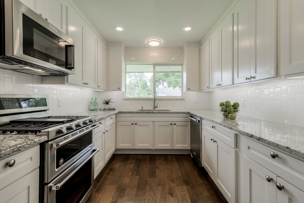 Photo of a traditional u-shaped kitchen in Dallas with shaker cabinets, white cabinets, white splashback, subway tile splashback, stainless steel appliances, medium hardwood floors and brown floor.