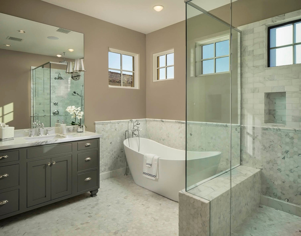 This is an example of a transitional bathroom in Phoenix with marble benchtops, white tile, a freestanding tub and grey cabinets.